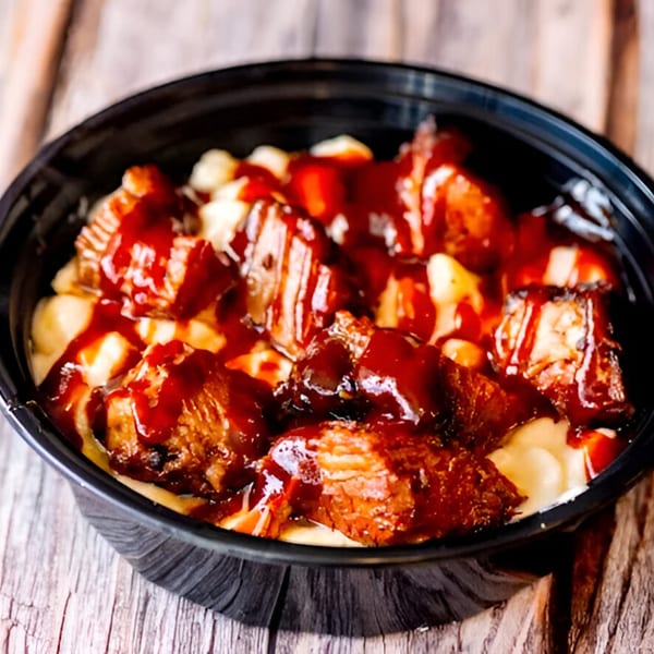 Mac Daddies' mac and cheese topped with BBQ brisket and sauce in a black bowl.
