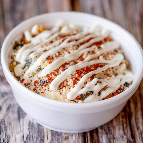 Mac Daddies' mac and cheese in a white bowl, topped with white sauce and red seasoning.