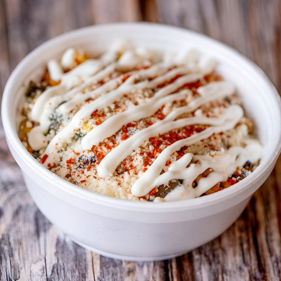 A white bowl of Mac Daddies mac and cheese, topped with white sauce and red seasoning.