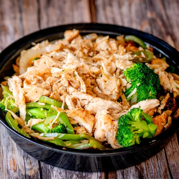 A black bowl filled with shredded chicken, green bell peppers, and broccoli florets on a wooden surface.
