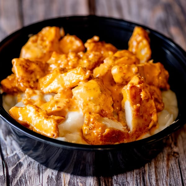 Mac Daddies' buffalo chicken mac and cheese in a black bowl on a rustic wooden table.
